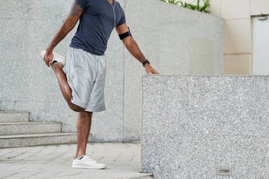 Müzik ve çalıştırmadan önce kentsel arka planda bacaklarını esnetiyor giyim tanınmaz Erkek atlet