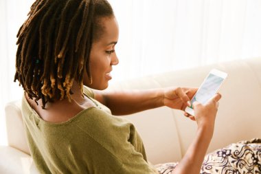 Genç ve güzel kadın kanepe ve manifatura içinde hareket eden telefon dinleniyor 