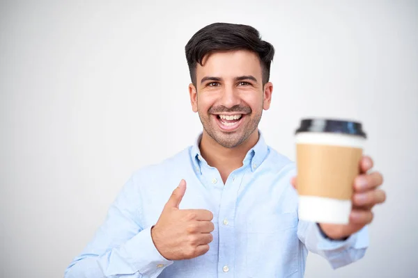 使い捨て可能な一杯のコーヒーを保持していると親指の分離の白い背景を示す幸せな若者の肖像 — ストック写真