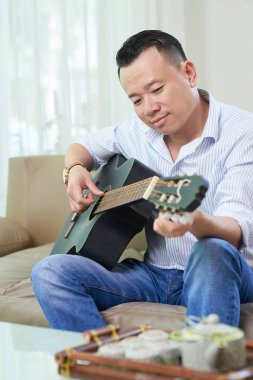 Gülümseyen yakışıklı Asya adam gitar evde oynarken zevk