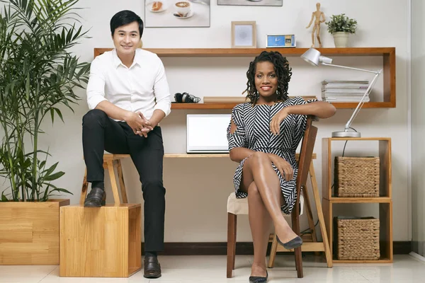 若いアジア系のビジネスマンと美しいアフリカ実業家一緒に職場で座っていると笑顔 — ストック写真
