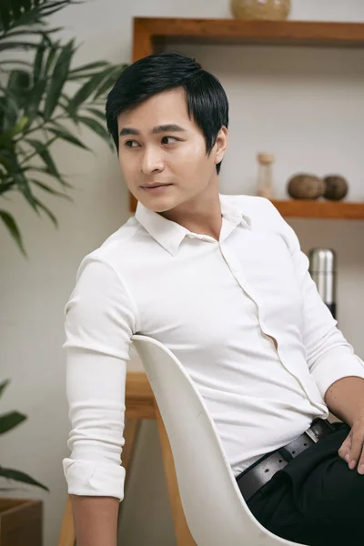 Young office worker in white shirt sitting on chair at office and looking away