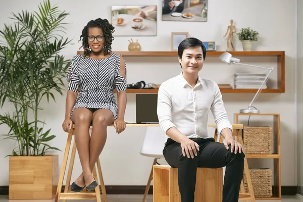 フォーマルウェアのスツールに腰掛けて 彼の女性のパートナー オフィスの机の上に座って 笑顔で笑顔のアジア系のビジネスマン — ストック写真