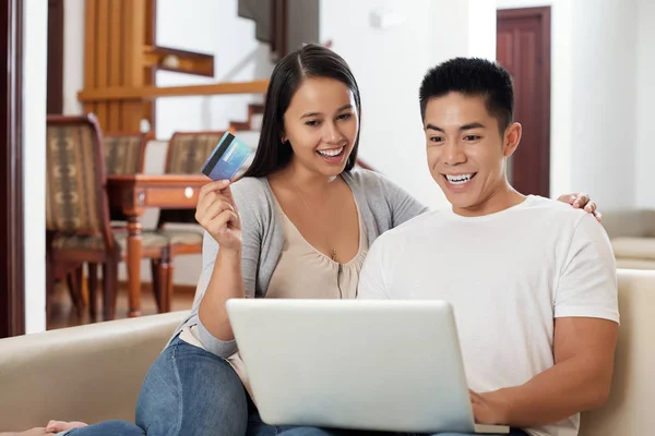 愉快的年轻混血夫妇与笔记本电脑坐在沙发上 网上购物 — 图库照片
