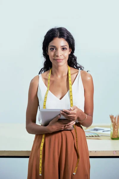 年轻女裁缝的肖像与磁带措施在她的脖子站在时尚的衣服和拿着数字平板电脑在工作室 — 图库照片