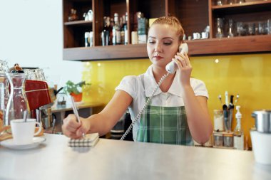 Genç kadın çekici notlar düzenin kafede istemci ile telefonda konuşurken önlük