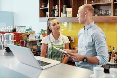 Genç kadın kahve dükkanı ayakta sayaç tablet ve dizüstü bilgisayar ile işveren dinlerken önlük