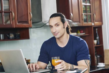 Bardak portakal suyu zevk ve onun laptop e-postaları kontrol yakışıklı genç adam portresi