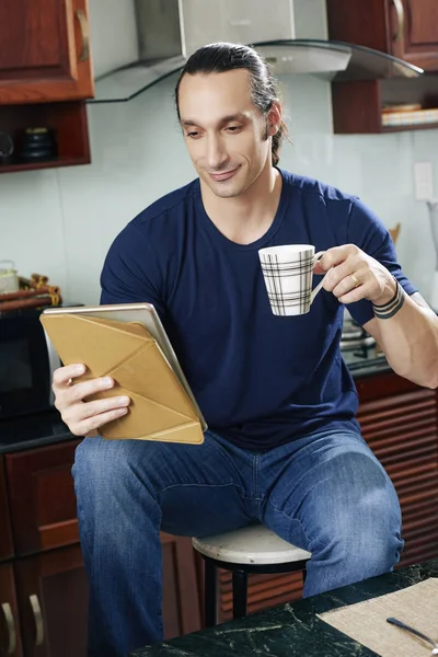 コーヒーを飲むと タブレット コンピューターのニュースを読んで若い男の笑みを浮かべてください — ストック写真