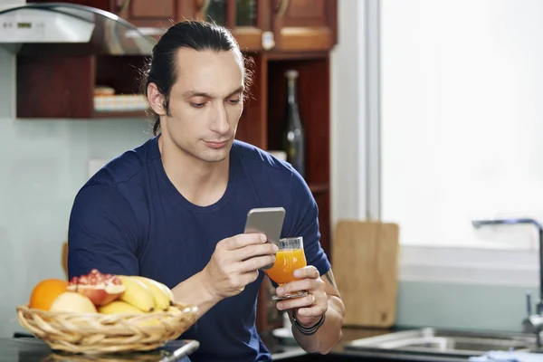 Joven Guapo Serio Con Vaso Jugo Naranja Comprobando Las Noticias — Foto de Stock