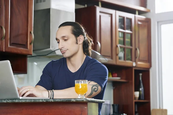 Positiv Ung Man Dricka Saft Och Arbetar Laptop Sitt Kök — Stockfoto