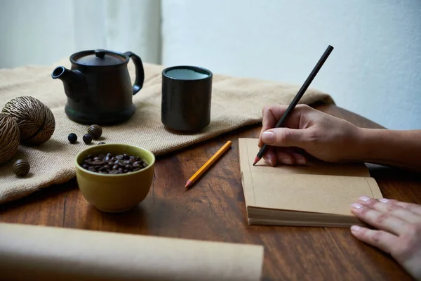 在木桌上用铅笔在打开的笔记本上写字的妇女 — 图库照片