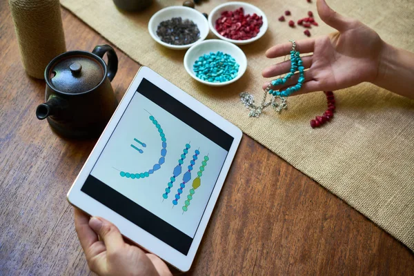 デジタル タブレットのビーズ織りと手作りのネックレスを作るユーザー マニュアルを探して 彼女のテーブルで働く女性 — ストック写真