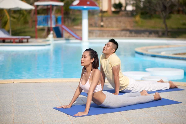 年轻的亚洲夫妇一起在室外游泳池附近的垫子上锻炼 — 图库照片