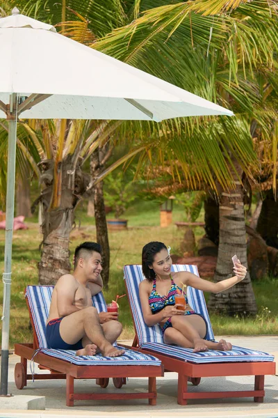 ブラブラしてカクテルを飲んで 夏の休暇中に携帯電話で自分自身を撮影の上に横たわる美しいカップル — ストック写真