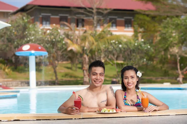 水泳しカクテルを飲んで 夏のリゾート地で新鮮な果物を食べて幸せなアジアのカップルの肖像画 — ストック写真