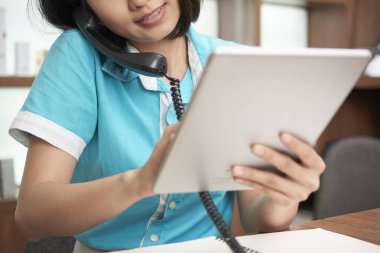 İstemci ile telefonda konuşurken tablet kullanarak Resepsiyon çağdaş genç kadın