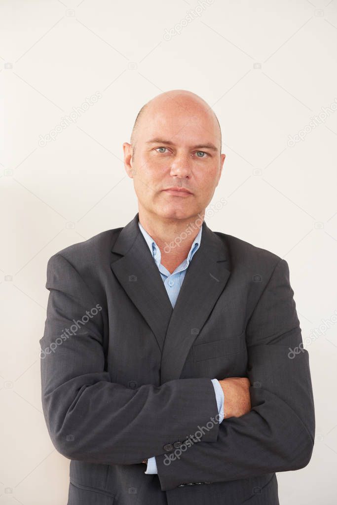 Portrait of confident balded mature businessman in black jacket standing with arms crossed on white background