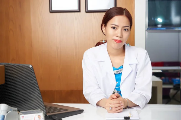 年轻的亚洲医生坐在她的工作场所与笔记本电脑在办公室的肖像 — 图库照片