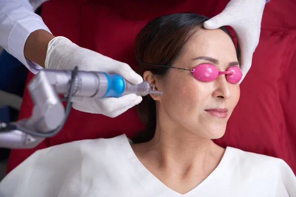 妇女正在健康中心接受抗衰老超声手术 她躺在防护眼镜里 而美容师则使用激光 — 图库照片