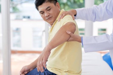 Ofiste çalışırken yetişkin Asya adam kol inceleyerek anonim pratisyen