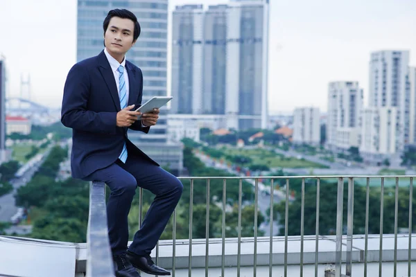 デジタル タブレットの彼の手の中と屋上で手すりに座って自信を持って若い起業家 — ストック写真