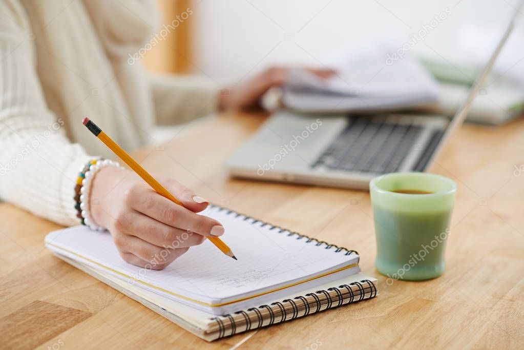 Close-up image of female office worker writing plans in notepad, selective focus