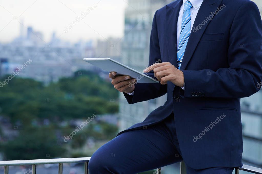 Cropped image of business executive using application on tablet computer when sitting on rooftop