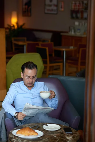 Vietnamese entrepreneur with morning coffee in restaurant and reading newspaper