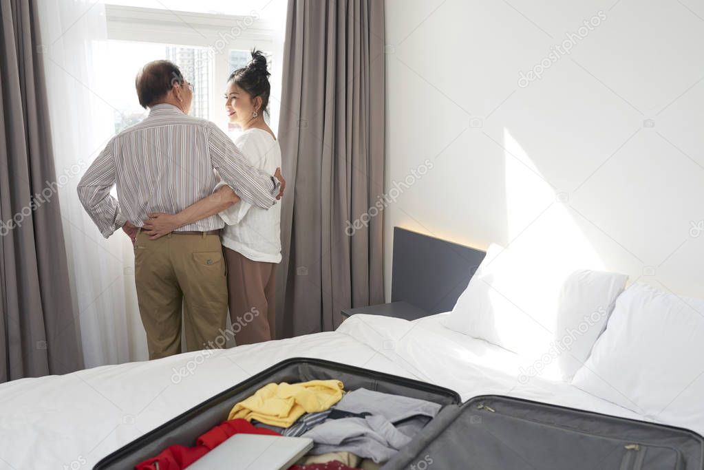 Smiling senior couple in love standing at hotel window and looking at each other