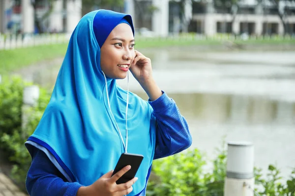 Красивая Индонезийская Женщина Хиджабе Улыбается Слушает Музыку Наушниках Держит Мобильный — стоковое фото