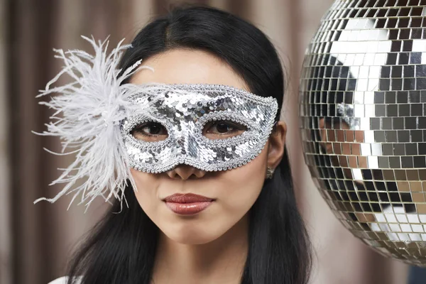 Pretty young Asian woman in silver sequins mask standing at disco ball