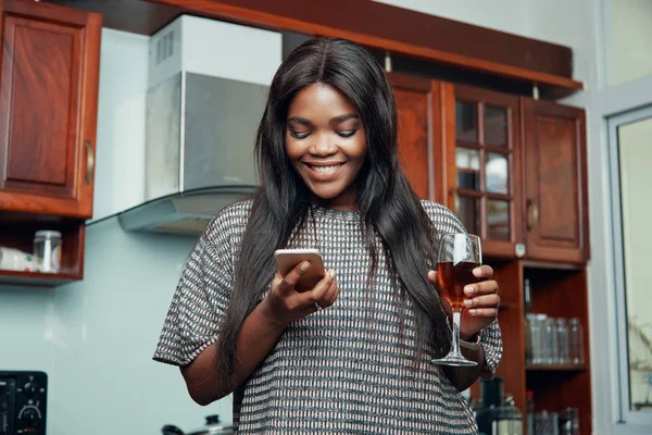 微笑快乐的年轻黑人妇女在智能手机里喝酒和阅读信息 — 图库照片