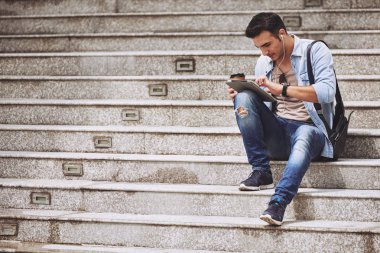 Açık havada dijital tablet üzerinde çalışırken kulaklık giyen genç adam