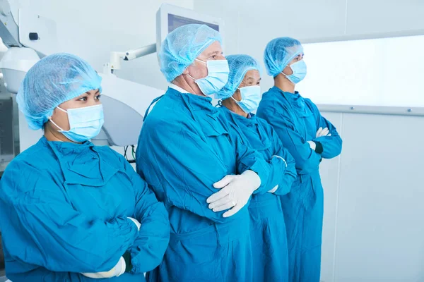 腕を越えて 一緒に手術に立ちながらよそ見を維持するマスクに外科チームの側面図 — ストック写真
