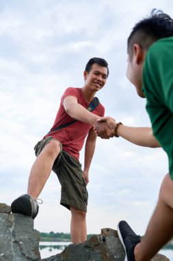 Onun arkadaşı yardım için el outstretching pozitif Genç Asyalı uzun yürüyüşe çıkan kimse