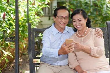 Smartphone cep telefonu ile iletileri okunurken gülümseyen mutlu yaşlı Asya Çift