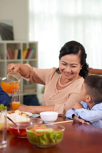 外婆在家庭聚餐时在孙子的杯子里倒果汁 — 图库照片