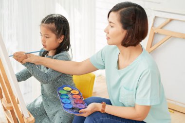 Küçük kız boya fırçası düzgün kullanmayı öğreterek profesyonel resim öğretmeni