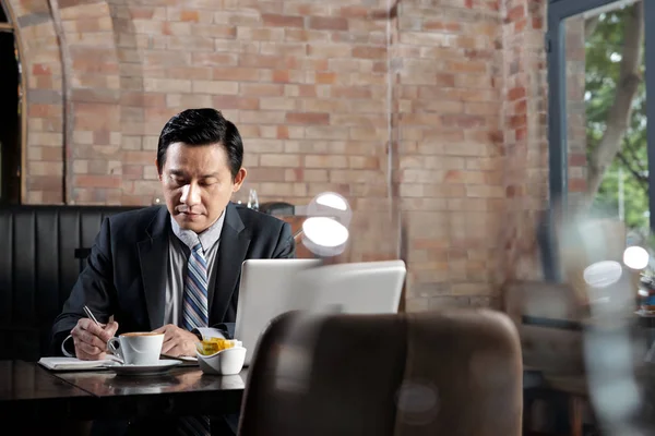 Dojrzałe Wietnamski Biznesmen Pisanie Planów Dzień Kiedy Jedzą Śniadanie Kawiarni — Zdjęcie stockowe