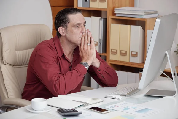 彼のコンピューターの画面に顔をしかめ 自分の机に座って事務所で問題と成熟したビジネスマン — ストック写真