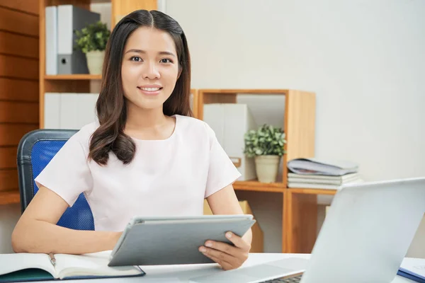 タブレットとカメラに笑顔でテーブルに座ってオフィスで働く美しい若いアジア女性 — ストック写真