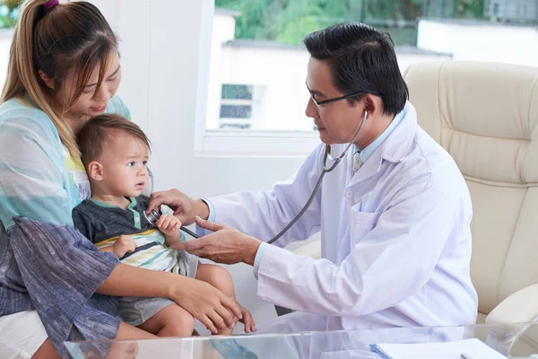 Küçük çocuğun kalp atışlarını dinlerken stetoskop kullanarak olgun Vietnamca doktor