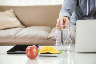 Taze meyve ve tablet pc dizüstü bilgisayar evde kullanırken bardak su işaret eden adamla masada Close-Up