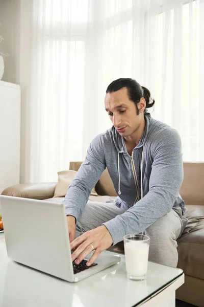 Jovem Concentrando Seu Trabalho Ele Digitando Laptop Bebendo Leite Enquanto — Fotografia de Stock