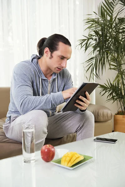 Joven Hombre Serio Usando Tableta Mientras Descansa Sofá Con Frutas — Foto de Stock