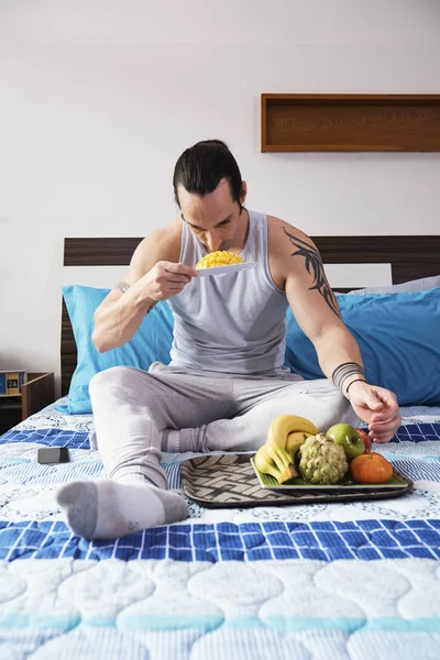 Joven Musculoso Con Tatuajes Sentado Cama Comiendo Mango Fresco Casa — Foto de Stock