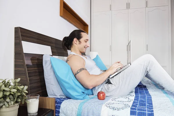 Hombre Feliz Sentado Cama Charlando Con Alguien Usando Computadora Portátil — Foto de Stock