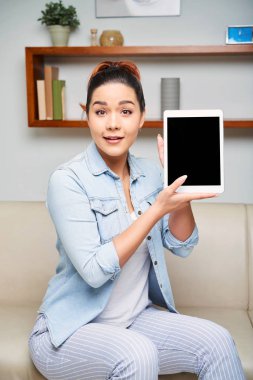 Kanepede oturan ve kamera ile sürpriz bakmak kadar dijital tablet gösterilen güzel kız portresi