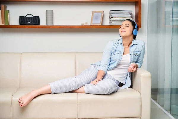 Young woman relaxing on sofa with her eyes closed and enjoying the music in her headphones